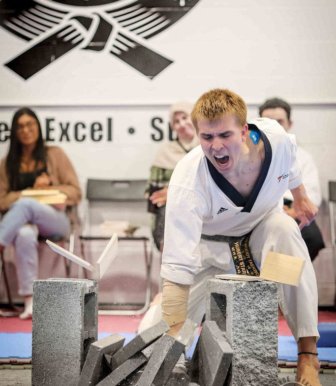 Adult student shouting as he breaks a stack of concrete at his black belt test