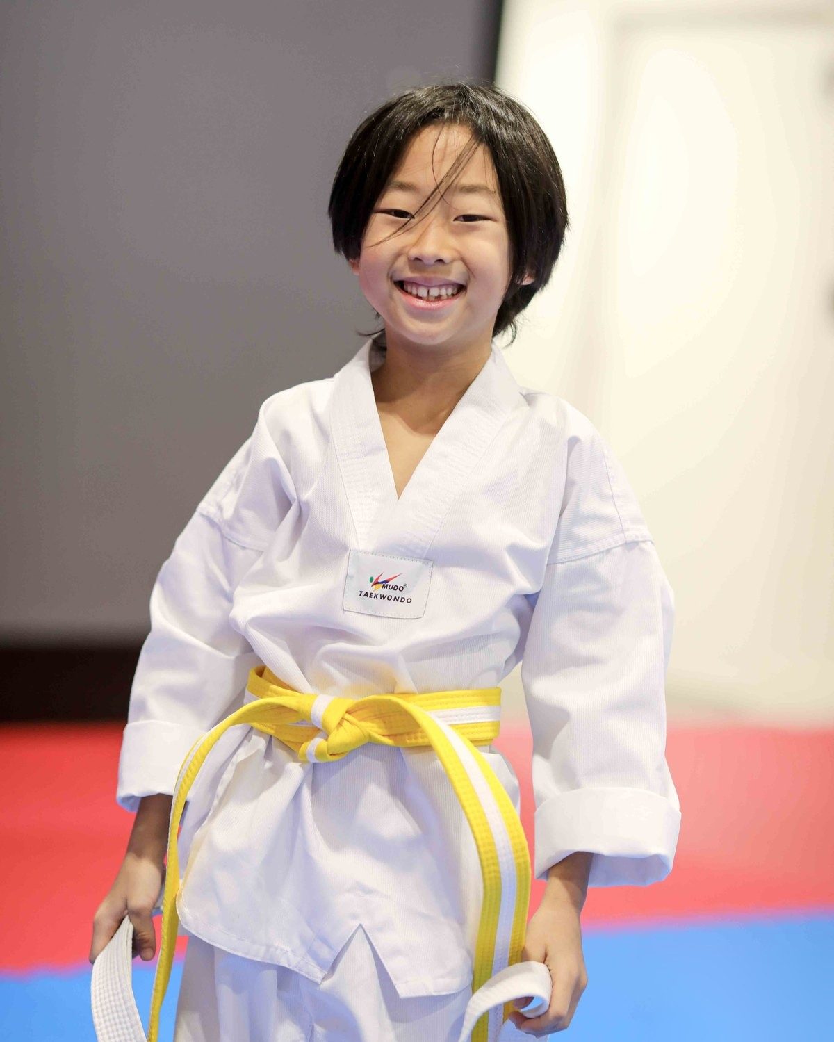 Smiling girl in a white uniform with her new yellow belt, holding her old white belt