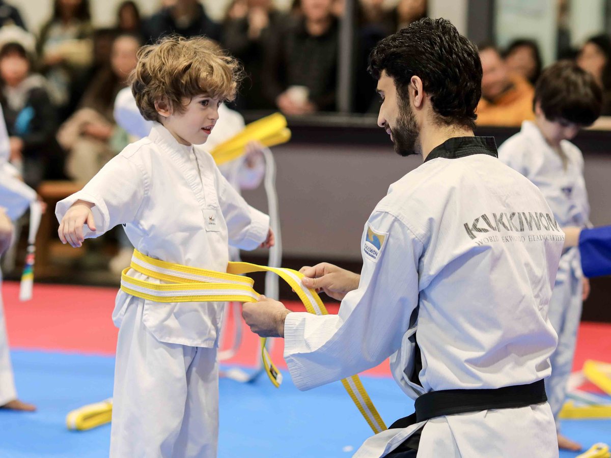 Instructor tying a new yellow belt on a young student