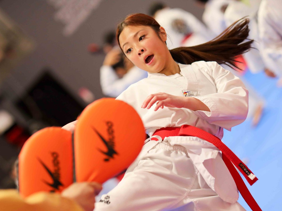 Red belt student side-kicking a pair of pads, eyes locked on the target, at a belt test