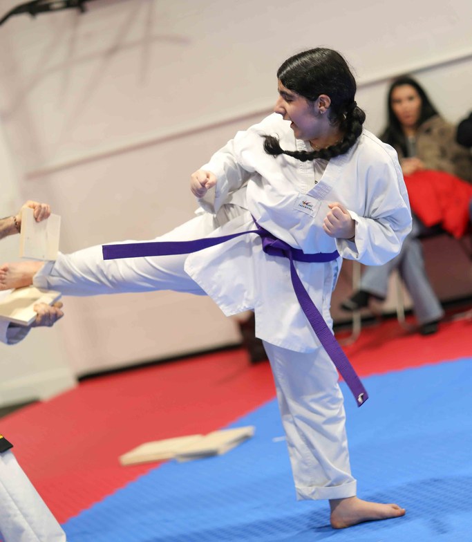 Purple belt student breaking a board with a side kick at a belt test