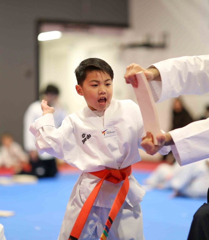 Orange belt boy breaking a board with a punch, instructor holding the board