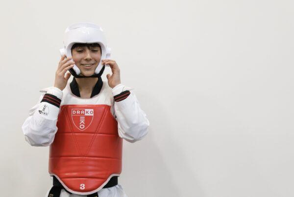 A smiling student fastening her head guard and chest protector before sparring