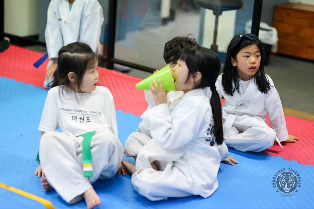 A young taekwondo student yelling into a green cone while classmates watch