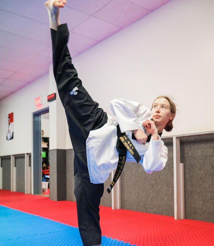 Teen Taekwondo student holding a vertical kick at full height in the studio